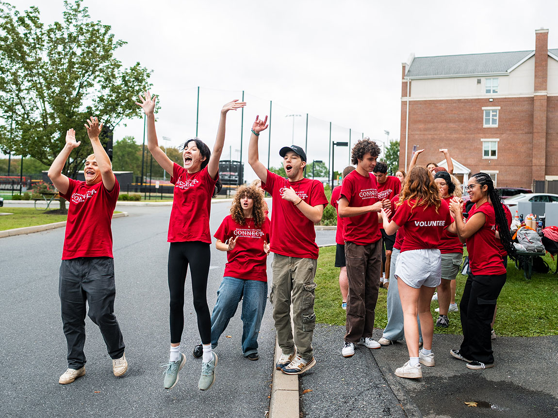 A group of college students in red T-shirts welcomes new students on move-in day